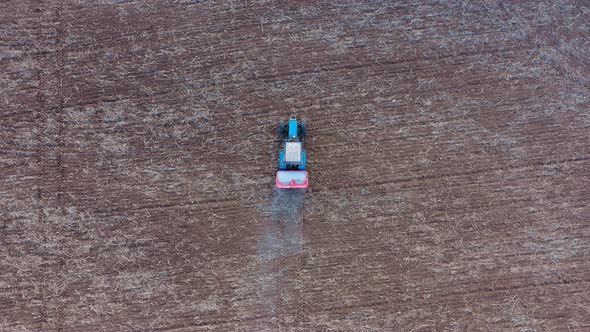 Aerial Flying Above Tractor With A Trailer Sprays Fertilizer On A Rural Field