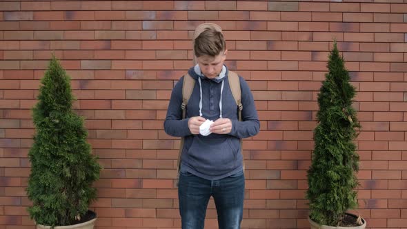 Caucasian Young Man with a Guitar on the Back Is Putting on a Medicinal Mask alt