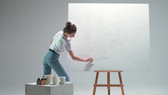 Back View Female Artist Applies a Layer of White Primer on a Large Canvas in a White Room a Talented alt