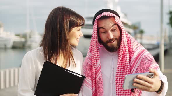 Smiling Arab Businessman Showing Something on Smartphone to His Attractive European Female Assistant alt