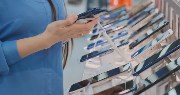 Hand of a Woman Holding a New Smartphone Near the Storefront in an Electronics Store alt