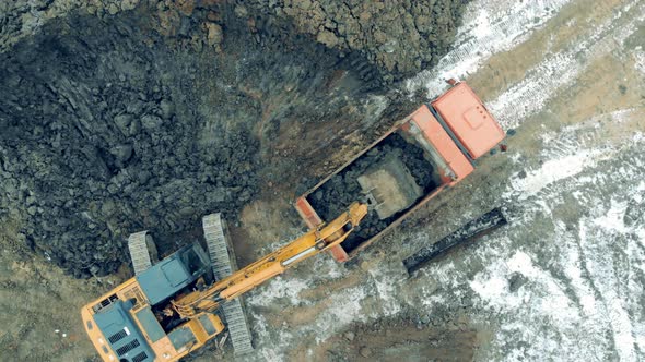 Working Excavator Loads a Truck with Stones at a Career alt