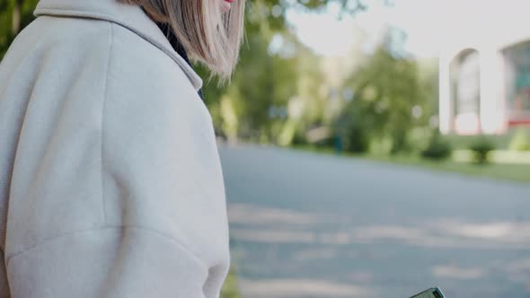 Girl Sits on a Park Bench Looking at the Phone Waving to a Friend and Smiling alt
