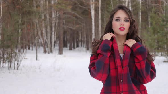 Young Woman with Wavy Hair Standing and Touching Face in Winter Forest