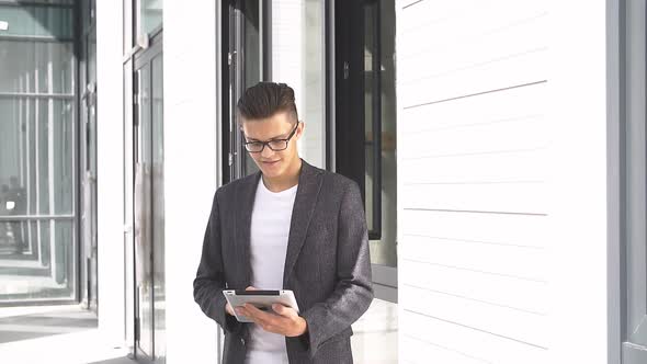Young Businessman Uses Tablet on Background of Modern Building.
