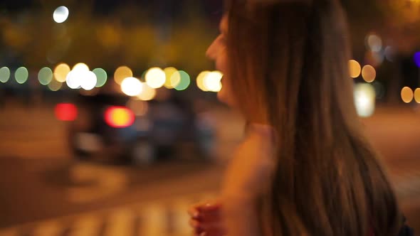 Teenage girl walking along city street at night, looking over shoulder and making faces at camera