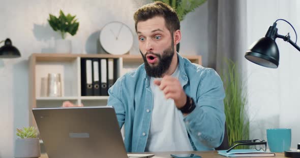 Bearded Guy Recieving Good News on Computer and Enjoying from Results with Raised Hands alt