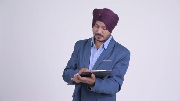 Bearded Indian Sikh Businessman Talking While Reading on Clipboard alt