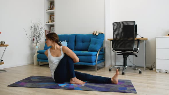 Young Woman Does Yoga At Home, Sits In Marichi Pose 