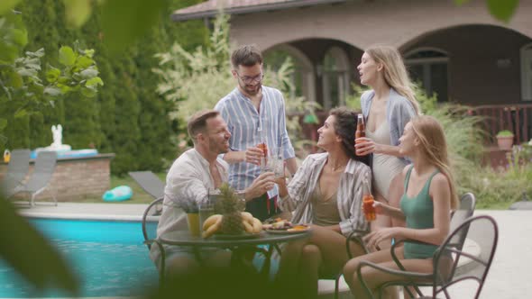 Group of happy young people cheering with cider by the pool in the garden