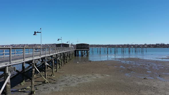 a low angle drone view during low tide. The drone camera dolly in next to an empty wooden pier on th alt