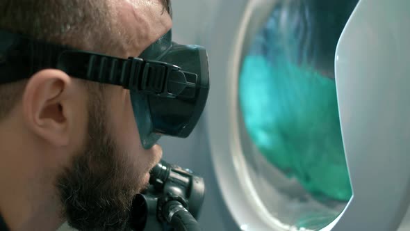 Man in a scuba suit looks into a broken washing machine. Close-up