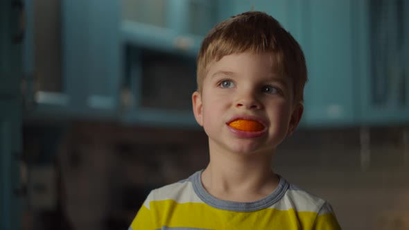 Preschool Blonde Boy Playing with Orange Peels in His Mouth. Smiling Kid with Orange Fruit in Mouth alt