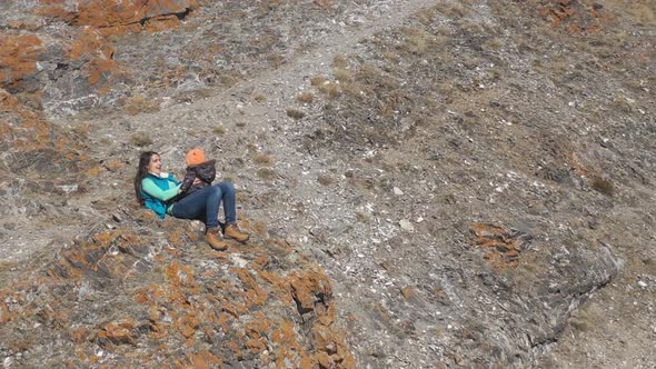 Aerial View of a Young Happy Mother Sitting on a Rock and Playing with Her Little Child.