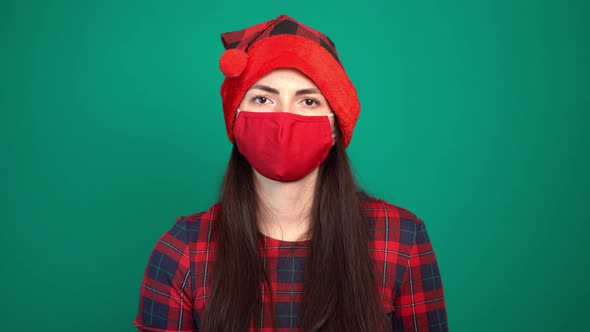 Portrait of Young Woman with Red Medical Face Mask and Santa Hat, Looking at Camera alt