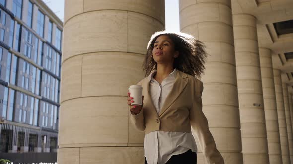 Young Woman Walks Confidently with Cup of Coffee to Office alt