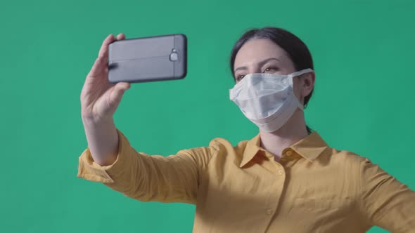 Young woman wearing a surgical mask and taking selfies with her smartphone