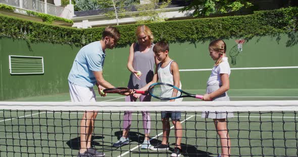 Caucasian father and mother teaching their kids to play tennis at tennis court on a bright sunny day alt