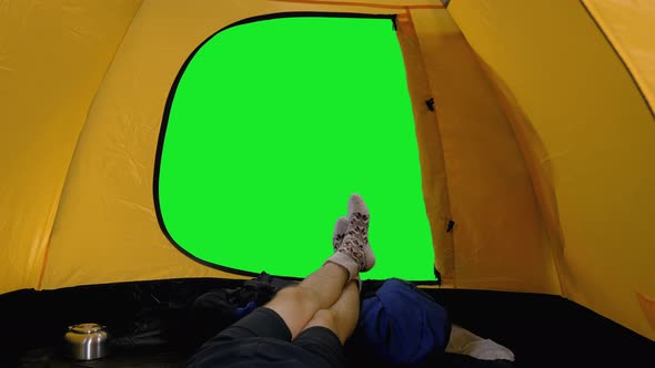 Camper Lying in Open Tent, View of his Legs in Woolen Socks against Green Screen Background