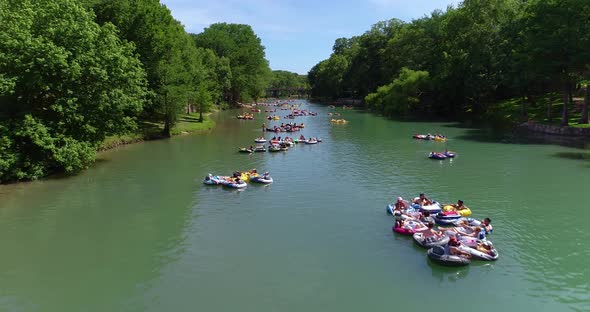 People tubing in groups down the Guadalupe river waving to the camera. This shot was taken in Canyon alt