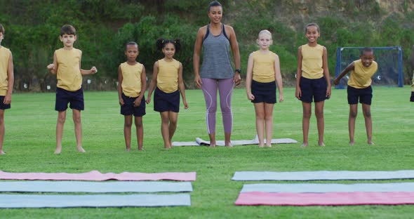 Mixed race female teacher and diverse group of schoolchildren jumping and smiling outdoors alt
