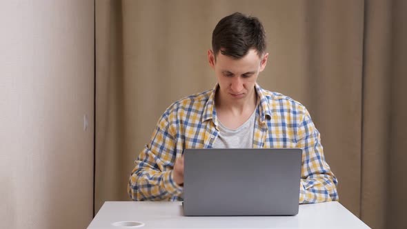 Young Man Angry Typing on Laptop at Table alt