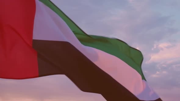 Close-up of the flag of the United Arab Emirates waving in the wind against a cloudless blue sky.