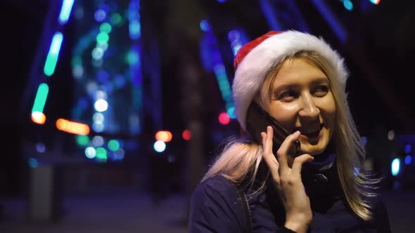 a woman chatting on her smartphone wearing a Santa hat is a night city. alt