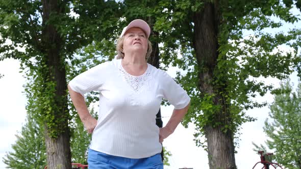 Elderly Grandmother with Low Back Pain During a Morning Workout in the Park alt