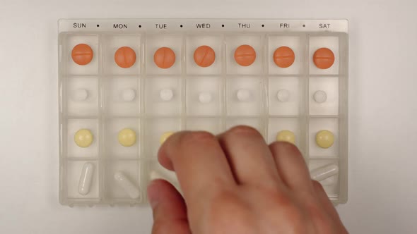 Male hand takes a pill from a plastic pill organizer