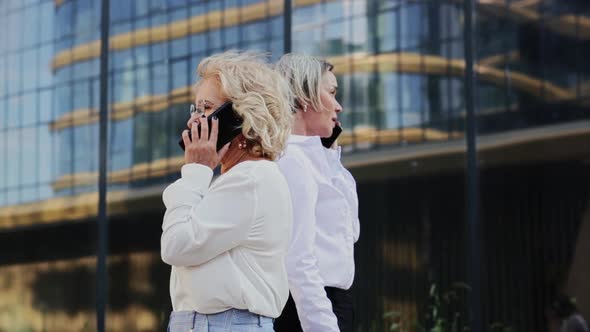 Businesswomen Talking on Mobile Phones While Walking By Office Building