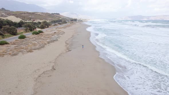 Drone footage of a woman running along the ocean coastline and leaving footprints in the sand. alt