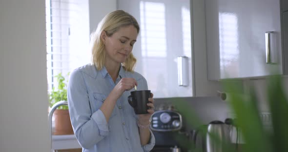 Blond woman standing stirring in coffee cup