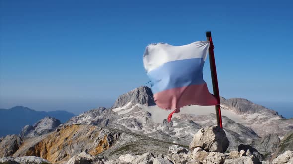 Slow motion footage of a tattered Russian flag developing in the wind. In the background is a blue s alt