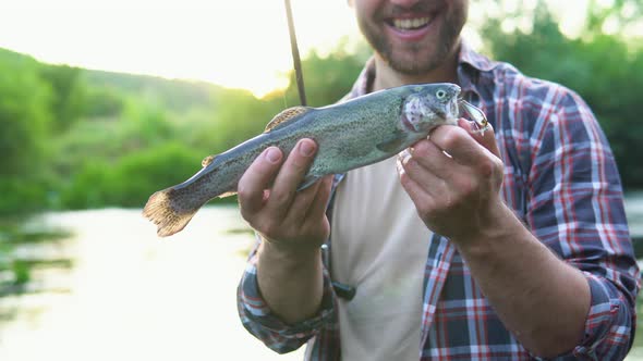 Fisherman Rests on the River and Catches Trout Smiles and Shows the Fish in the Camera alt