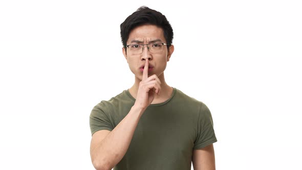 Portrait of Brunette Chinese Man Wearing Glasses and Basic Tshirt Doing Shh Gesture with Index alt