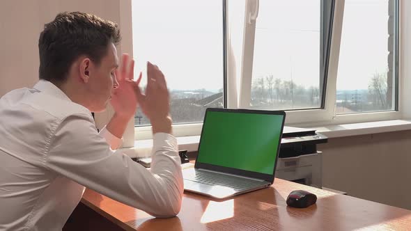 A Frustrated Caucasian Man Sits at a Desk in Front of a Computer with a Green Screen in the Office alt