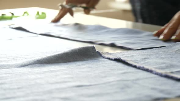 Female Seamstress Hands with Manicure Cut Off Blue Colored Fabric with Special Sewing Scissors alt