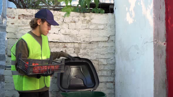 Food Waste at Retail. A supermarket worker throws spoiled rotten unsold vegetables into a dumpster alt