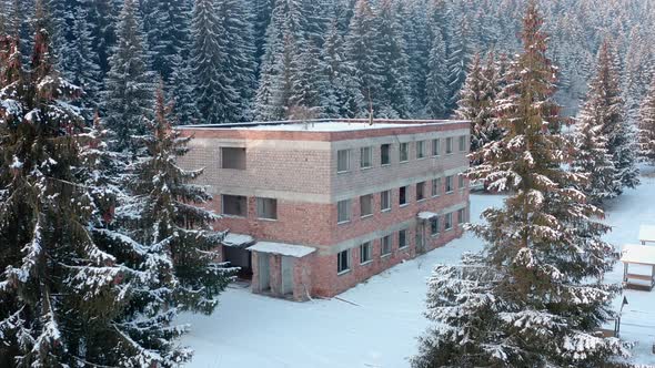 Degraded Building Surrounded By Snowy Pine Trees In Winter Forest - Wide Shot alt
