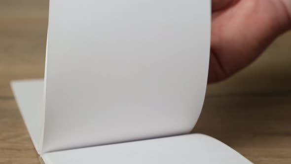 Hand flipping empty notebook pages on a wooden table. Close up. 4k alt