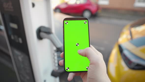 Slow motion green screen smart phone tapped with electric car charging on street