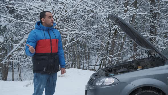 Man Standing on Road Near Broken Car and Trying To Catch Help on Winter Forest Road