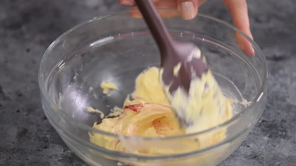 Close Up of Baker Hand Adding Food Color Into Bowl with Batter Cream and Mixing with a Silicone