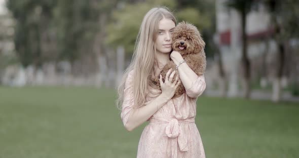 A beautiful girl, blonde, is holding a poodle dog in her hands