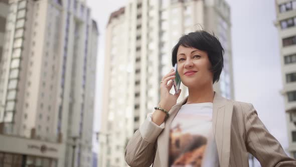 Business Woman Talking on the Phone Makes a Deal Against the Background of Houses in the City