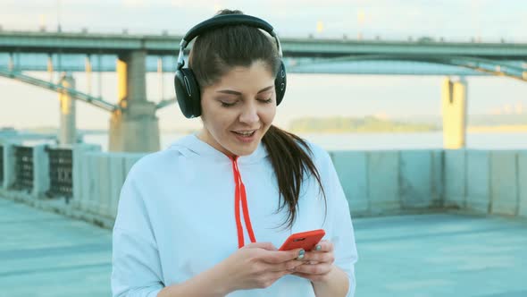 A Beautiful Girl in a White Sweater and Headphones Is Preparing for a Morning Run. alt