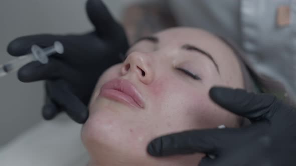 Closeup Beautician Hands in Gloves Massaging Botox Injections on Face of Slim Young Woman alt