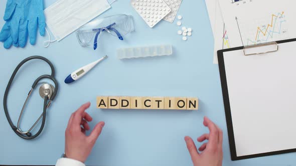 Word addiction is made up of wooden letters on the medical table, a view from above. alt