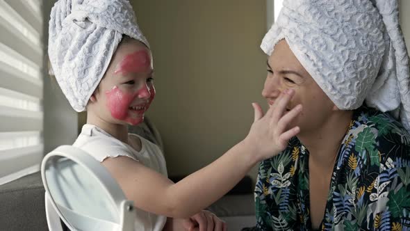 Little Girl with a Cosmetic Mask on Her Face Helps Her Mother To Make a Cosmetic Mask alt